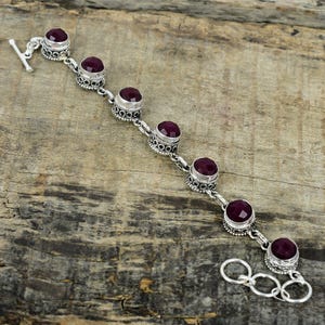 May include: A silver bracelet with seven round, dark purple gemstones. The bracelet has a toggle clasp.