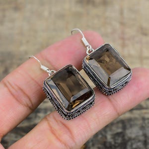 May include: A pair of silver earrings with a rectangular smoky quartz gemstone in each. The earrings have an intricate filigree design around the stones.