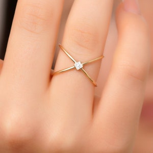 May include: A gold ring with a small diamond in the center. The ring has a criss-cross design.