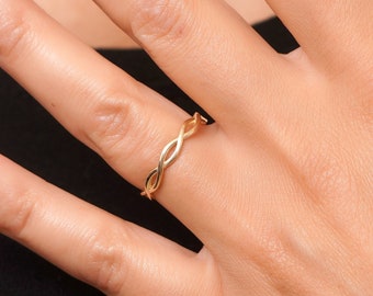 May include: A gold braided ring on a finger.