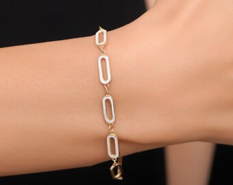 Peut inclure: Un bracelet en or avec des maillons ovales en émail blanc. Le bracelet est porté au poignet.