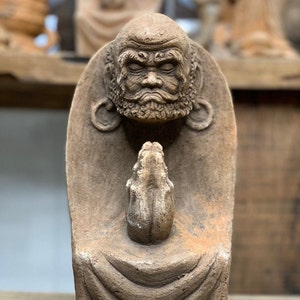 May include: A terracotta statue of a meditating figure with closed eyes and hands clasped in prayer. The figure is wearing a robe and has a detailed face with a beard.