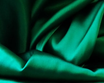 May include: Close-up of emerald green fabric with soft folds and shadows. The fabric has a lustrous sheen, suggesting a satin or silk material. The folds create a sense of depth and texture, highlighting the rich color.