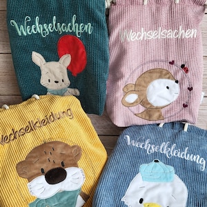 Könnte beinhalten: Vier Kordelzugbeutel aus Cord in Türkis, Rosa, Gelb und Blau. Jede Tasche hat ein gesticktes Tierdesign und Text. Die türkisfarbene Tasche hat ein Kaninchen mit einem roten Ballon. Die rosa Tasche hat ein Reh. Die gelbe Tasche hat einen Otter. Die blaue Tasche hat eine Ente.