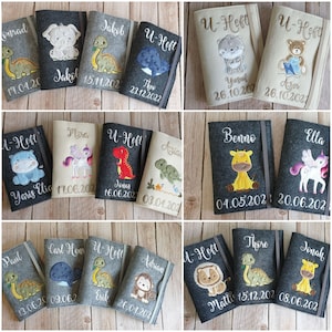 K&ouml;nnte beinhalten: Eine Sammlung personalisierter Baby-Notizb&uuml;cher mit gestickten Tierdesigns. Die B&uuml;cher zeigen Namen und Daten, mit verschiedenen Tieren wie Dinosauriern und Einh&ouml;rnern. Die Einb&auml;nde sind in Grau- und Beiget&ouml;nen gehalten.