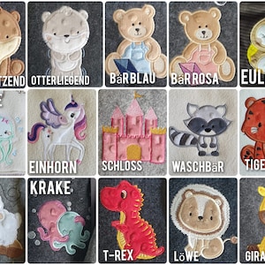 K&ouml;nnte beinhalten: Eine Sammlung von aufgestickten Filzaufn&auml;hern mit verschiedenen Tieren und Objekten. Designs umfassen einen Otter, B&auml;ren, Eule, Qualle, Einhorn, Schloss, Waschb&auml;r, Tiger, Schaf, Krake, T-Rex, L&ouml;wen und Giraffe. Jedes Patch hat ein deutsches Wort.