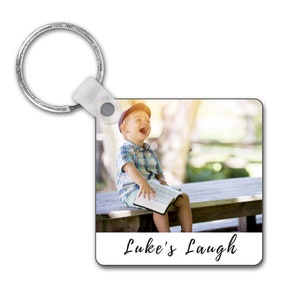 Könnte beinhalten: Ein quadratischer Foto-Schlüsselanhänger mit einem Bild eines jungen Jungen, der lacht, während er auf einer Holzbank sitzt. Der Text "Luke's Laugh" ist unten auf dem Schlüsselanhänger gedruckt.