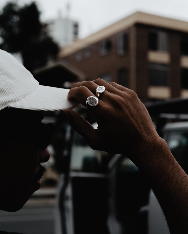 May include: A person wearing a white hat and two silver rings with intricate designs on their fingers.