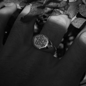 May include: A silver signet ring with a rose design engraved on the face.