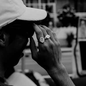 May include: A person wearing a white corduroy baseball cap with two silver rings on their finger.
