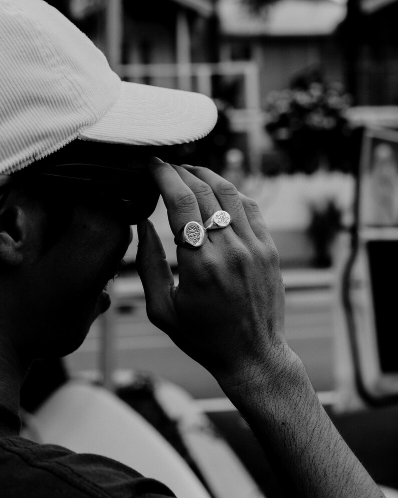 May include: A person wearing a white corduroy baseball cap with two silver rings on their finger.