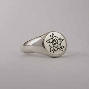 May include: A silver signet ring with a rose design engraved on the top.