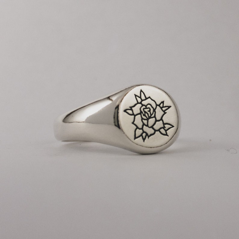 May include: A silver signet ring with a rose design engraved on the top.