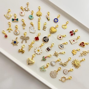 May include: A collection of gold-toned metal charms featuring various designs including hearts, flowers, animals, celestial symbols, food items, and letters. Each charm is equipped with a small lobster clasp for attachment to jewelry or accessories.
