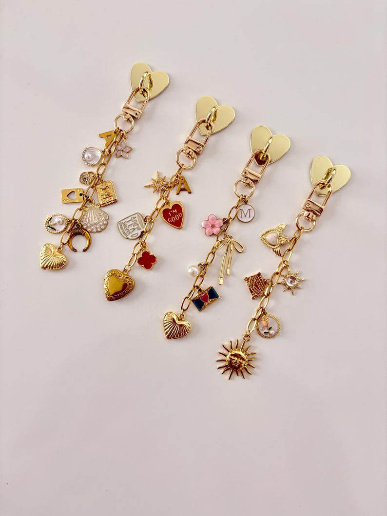 May include: Four gold-colored zipper pulls with heart-shaped tops and various charms. Charms include hearts, pearls, flowers, and a sun. The zipper pulls are on a white background.