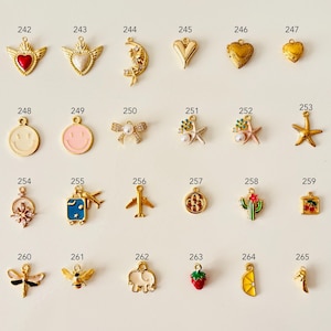May include: A collection of gold-toned charms with various designs, including hearts, a crescent moon, a smiley face, a bow, a starfish, a cactus, a strawberry, and a lemon slice. Each charm has a small loop for attaching to jewelry.