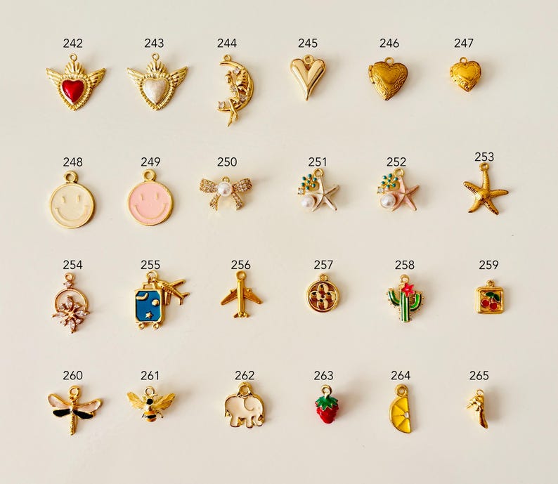 May include: A collection of gold-toned charms with various designs, including hearts, a crescent moon, a smiley face, a bow, a starfish, a cactus, a strawberry, and a lemon slice. Each charm has a small loop for attaching to jewelry.
