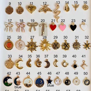 May include: A collection of 58 gold-toned and enamel charms with various designs, including hearts, moons, stars, bows, and suns. Some charms have colorful enamel details in red, blue, pink, and black. The charms are arranged in rows.