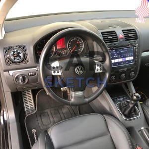 Puede incluir: Vista interior del salpicadero de un coche Volkswagen. El volante de cuero negro tiene un logotipo VW plateado en el centro. El salpicadero cuenta con indicadores, una pantalla digital y rejillas de ventilación. El interior del coche es negro.