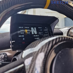 Könnte beinhalten: Nahaufnahme des Innenraums eines Autos, das ein Carbonlenkrad mit gelbem Streifen und ein digitales Display mit dem Buchstaben 'N' und verschiedenen Zahlen zeigt. Das Display zeigt 'N -0.01 1.00' und '35.8 -17 -10 31.1 1.1 RACE' an.