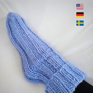 Pode incluir: Um par de meias de lã azul claro com um padrão de nervuras. As meias são dobradas na parte superior, revelando uma textura macia e fofa.