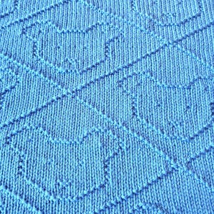 May include: Close-up of a knitted blue blanket with a geometric pattern. The blanket is a solid light blue color with a textured surface. The pattern consists of diagonal lines and shapes.