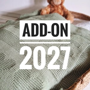 Op de afbeelding: Een saliegroene gebreide deken met een geometrisch patroon is opgevouwen in een rieten mand. De tekst "ADD-ON 2027" staat over de deken. Op de achtergrond staat een bruine teddybeer.