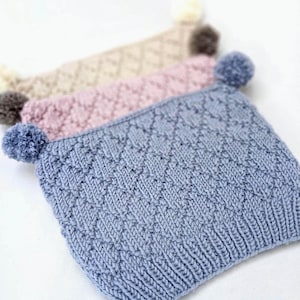 May include: Three knitted hats with pom-poms. The hats are in shades of blue, pink, and beige.