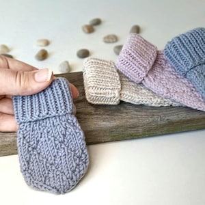 May include: Four knitted fingerless gloves in different shades of grey, pink, and beige. The gloves have a folded cuff and a textured knit pattern.