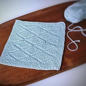 Puede incluir: Un paño de cocina de punto azul claro con un patrón texturizado. El paño de cocina está sobre una superficie de madera.