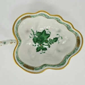 Pode incluir: Um prato de porcelana branca em forma de folha com um design floral verde e dourado. O prato tem uma alça e é perfeito para servir petiscos ou sobremesas.