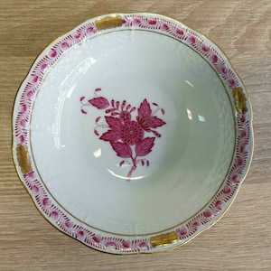 Könnte beinhalten: Eine weiße Porzellanschale mit einem rosafarbenen Blumendesign und goldenen Verzierungen. Die Schale hat einen gewellten Rand und einen erhöhten Rand.