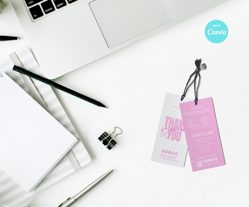 May include: Overhead shot of a workspace with a laptop, notepad, pen, and two clothing tags. One tag is white with pink text that says "Thank you". The other tag is pink with product information and care instructions.