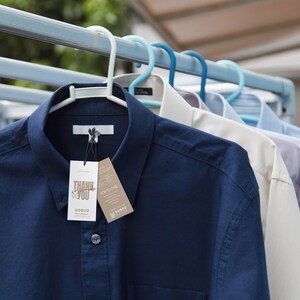May include: Several button-down shirts hanging on a clothesline. The shirts are in various colors, including navy blue, white, and light blue. A navy blue shirt in the foreground has a tag that says "THANK YOU".