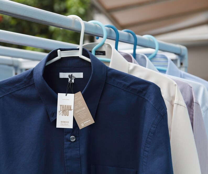 May include: Several button-down shirts hanging on a clothesline. The shirts are in various colors, including navy blue, white, and light blue. A navy blue shirt in the foreground has a tag that says "THANK YOU".
