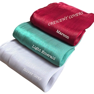 Op de afbeelding: Drie gevouwen stukken stof in bordeauxrood, licht smaragdgroen en zilvergrijs. De bordeauxrode stof heeft de tekst "CRESCENT COVERS" en "Maroon". De licht smaragdgroene stof heeft de tekst "Light Emerald". De zilvergrijze stof heeft de tekst "Silver Grey".