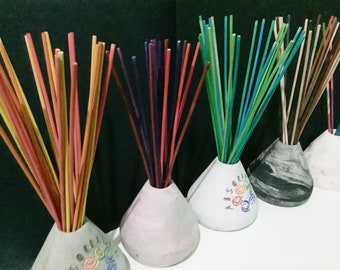 May include: Five ceramic diffuser bases with colorful wooden sticks. The bases are white, gray, and black with a swirl pattern. The sticks are red, orange, yellow, green, blue, purple, and brown.