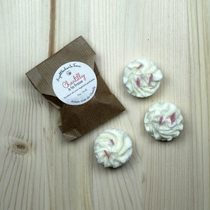 Peut inclure: Trois petits fondants de cire en forme de cupcakes, de couleur blanche avec un glaçage rose et des pépites. Les fondants de cire sont emballés dans un sac en papier brun avec une étiquette blanche qui indique "Chantilly à la fraise Fondant de cire végétale parfumée 52g 1.8 oz Artisan cire de Chantilly".