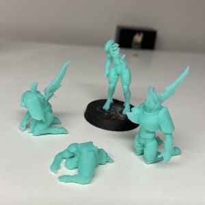 May include: Four miniature figurines made of a light green plastic. The figurines are in various poses, including standing, kneeling, and lying down. The figurines appear to be fantasy characters.