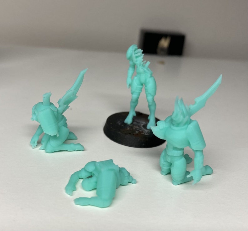 May include: Four miniature figurines made of a light green plastic. The figurines are in various poses, including standing, kneeling, and lying down. The figurines appear to be fantasy characters.