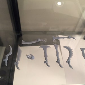 May include: A set of nine grey 3D printed fantasy weapons, including swords, daggers, and axes. The weapons are arranged on a white surface.