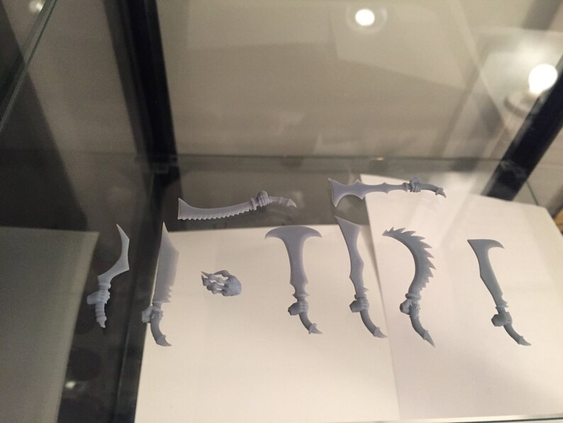 May include: A set of nine grey 3D printed fantasy weapons, including swords, daggers, and axes. The weapons are arranged on a white surface.