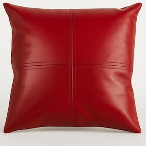 May include: Red leather pillow with a square design and stitched seams.