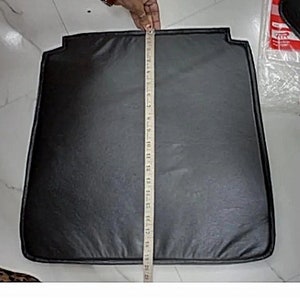May include: Black leather car seat cover with a black stitched border. The cover is being measured with a ruler.
