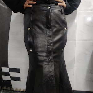 May include: A black leather skirt with a flared, mermaid-style hem. The skirt features a high waist, button details, and a tailored fit. The skirt is made of a shiny, smooth material.