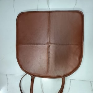 May include: Brown leather chair cushion with four stitched panels and two long ties.