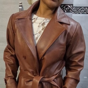 May include: A brown leather trench coat with a double breasted closure, a belt, and long sleeves.