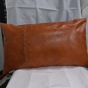 Könnte beinhalten: Ein braunes Lederkissen mit einem dekorativen Steppdesign. Das Kissen ist rechteckig und hat einen Reißverschluss.