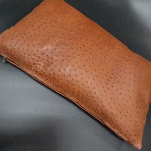 Peut inclure: Un coussin en cuir marron avec un motif peau d'autruche. Le coussin a une fermeture éclair.