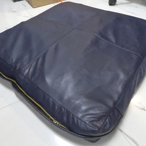 May include: A dark blue leather cushion with a gold zipper. The cushion is rectangular and has a quilted design.